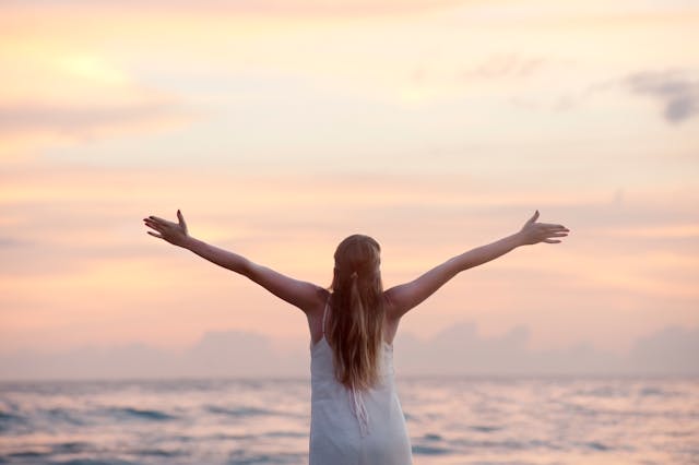 Woman extending her arms while looking at the ocean