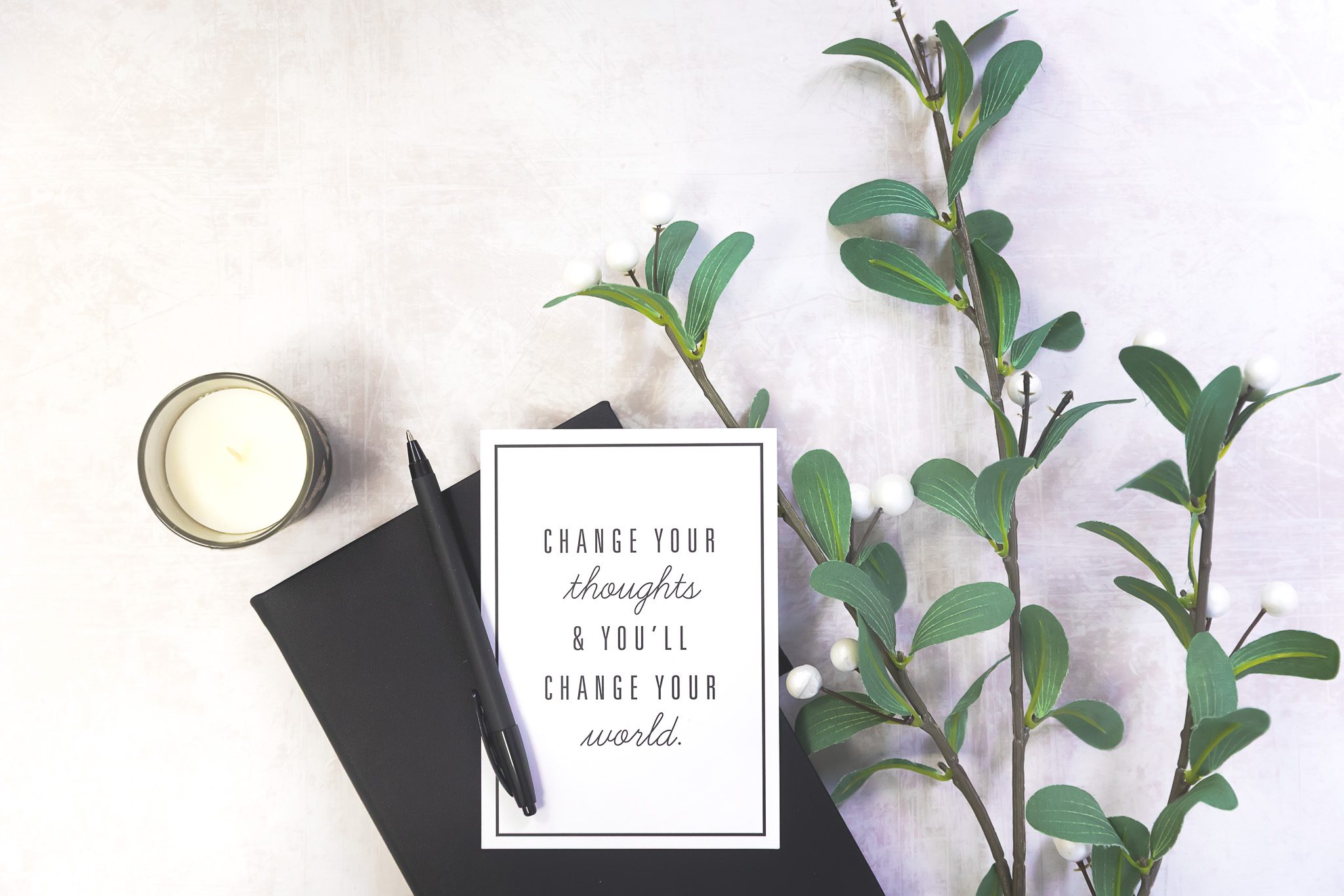 A motivational quote on paper, surrounded by flower stems, a notebook, and a candle