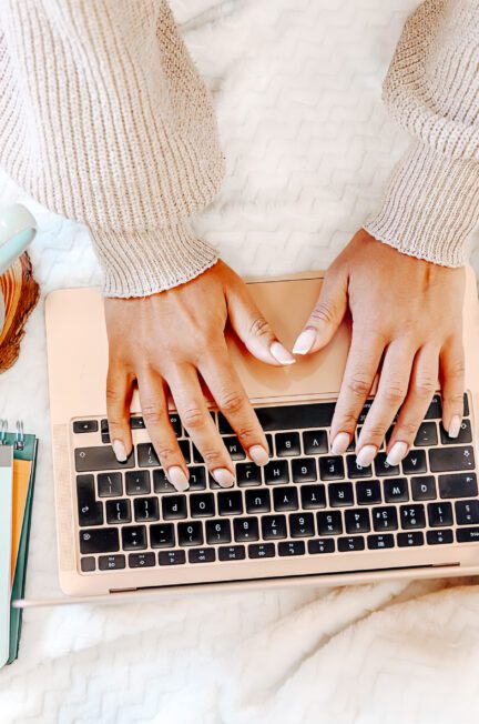 “Female typing on a laptop, with a phone, notebook, and cup of coffee nearby