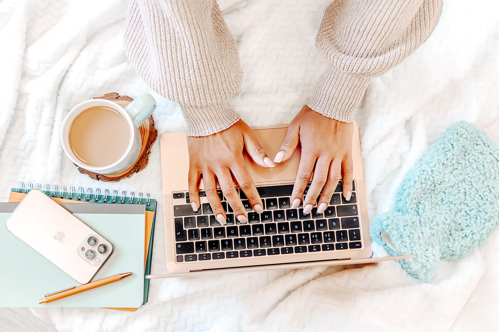 “Female typing on a laptop, with a phone, notebook, and cup of coffee nearby