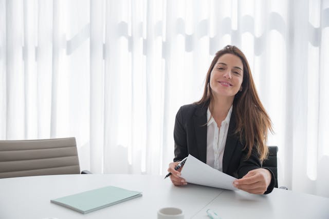 Woman in office smiling at the camera while holding a paper
