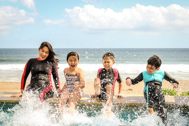 Mother and children seated on a pool edge, with the ocean behind them