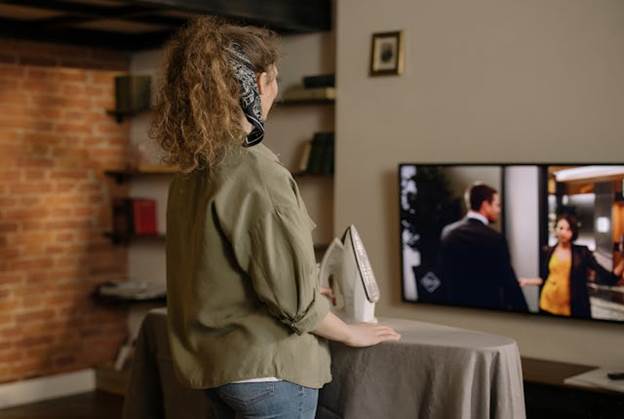 Woman ironing while watching television