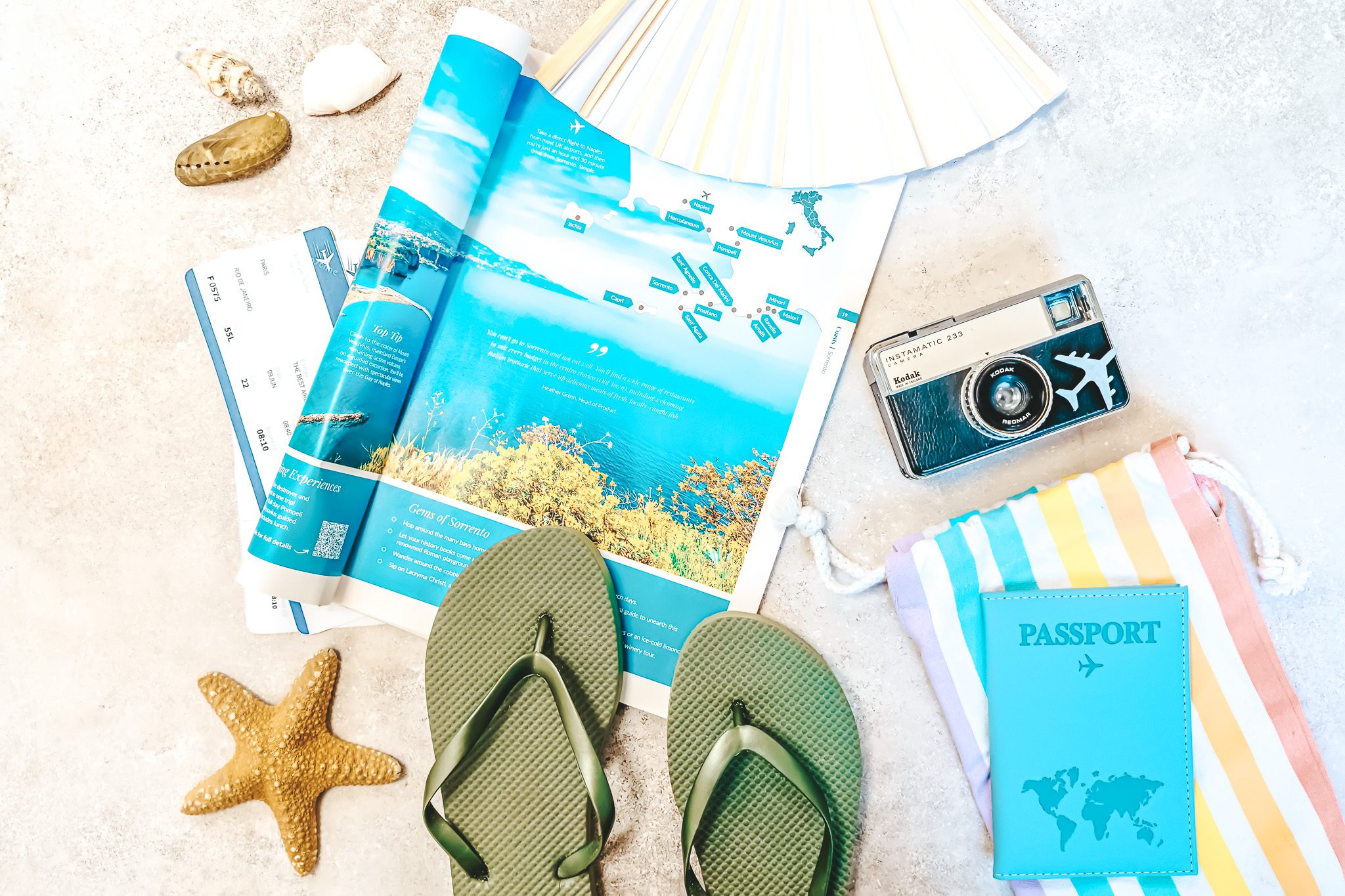 A camera, passport, flipflops, and magazine on the sand