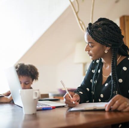 Mother working on her laptop at home while her daughter plays beside her