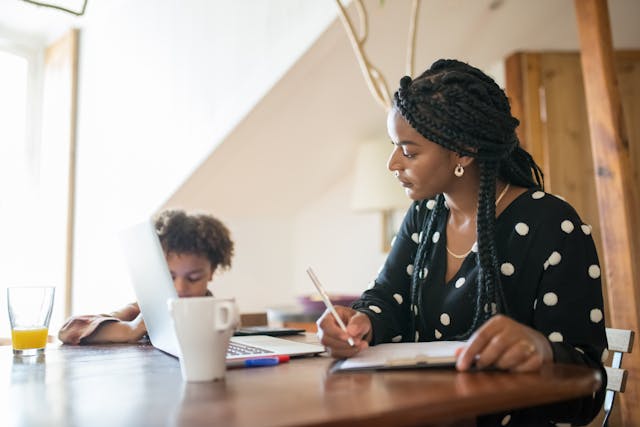 Mother working on her laptop at home while her daughter plays beside her