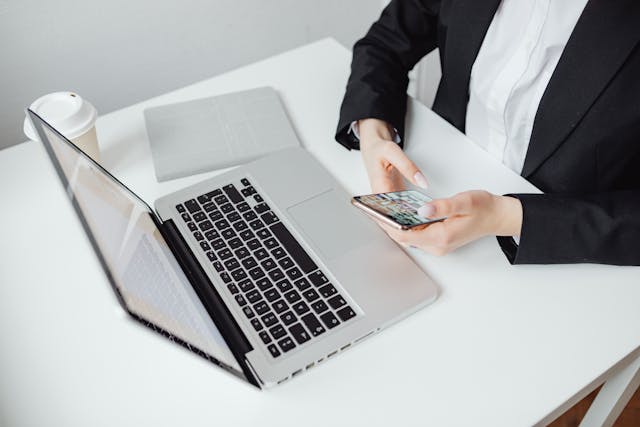 Cropped woman searching on her phone with a laptop in front of her