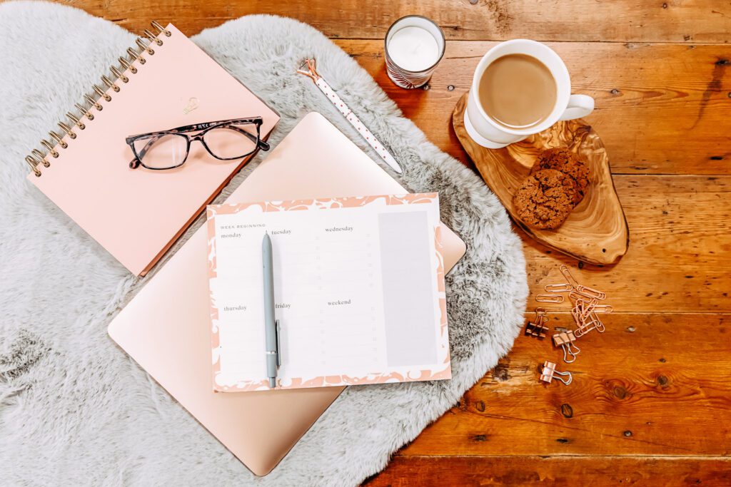 Planner on a laptop with a notebook, eyeglasses, and a cup of coffee nearby
