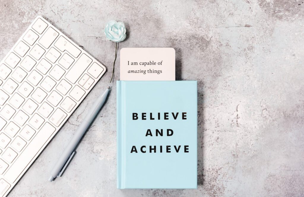 A notebook with a motivational quote, alongside a laptop and a small flower