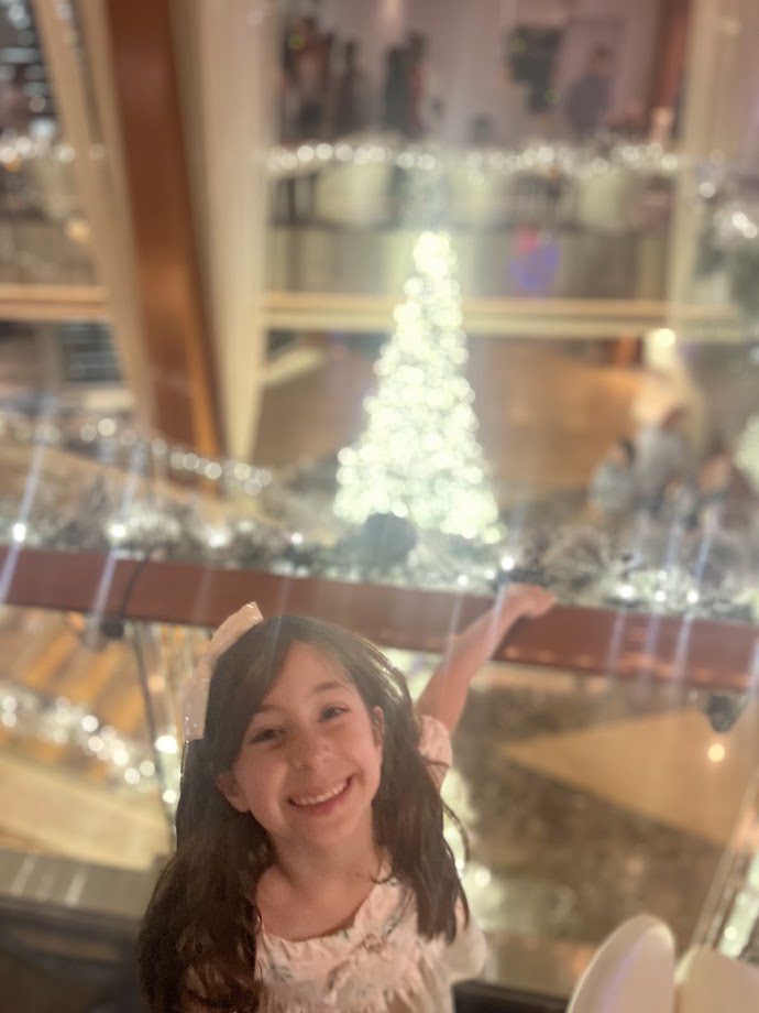 Close up of Melissas daughter smiling at the camera with a Christmas tree in a background