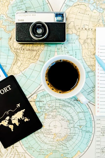 Close-up of a passport resting on a map, next to a cup of coffee, a camera, and a list
