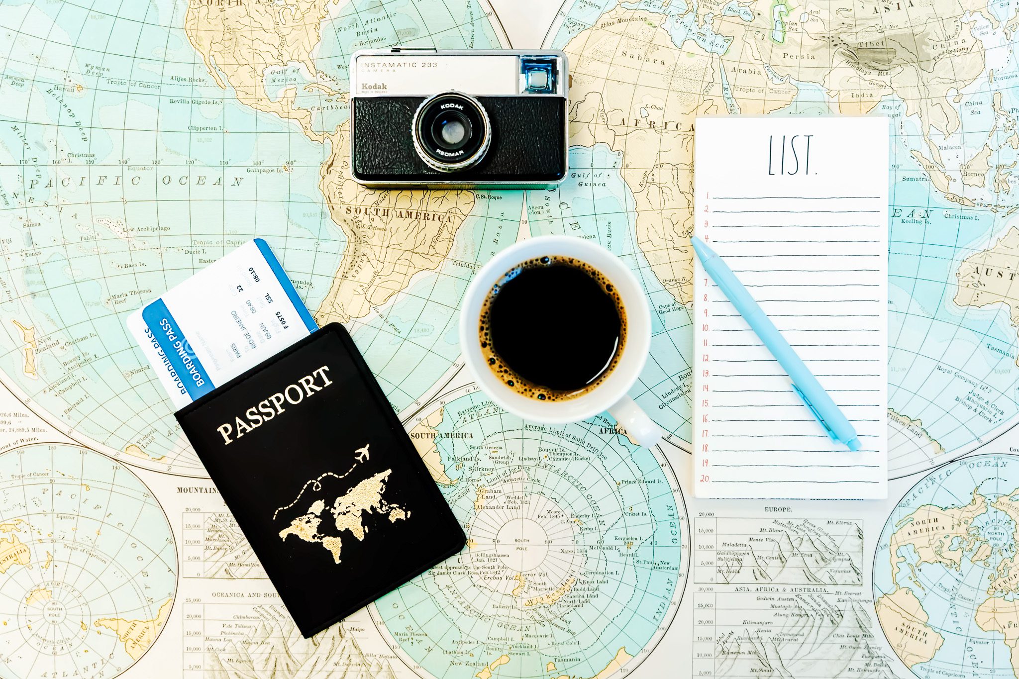 Close-up of a passport resting on a map, next to a cup of coffee, a camera, and a list