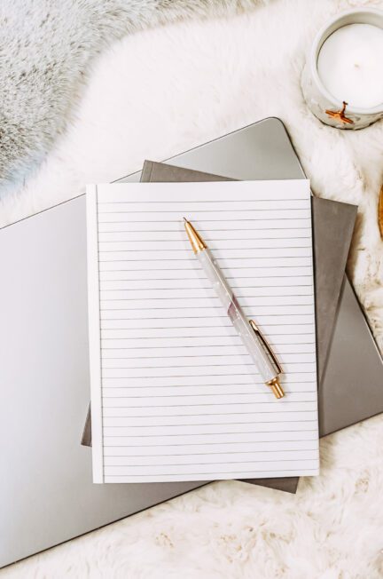 Notebook and pencil resting on a laptop beside a cup of coffee
