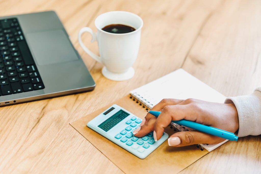 Woman using a calculator placed on top of a notebook, pen in hand