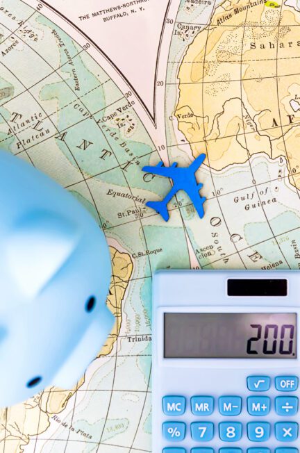 Piggy bank, toy airplane, and calculator on a world map