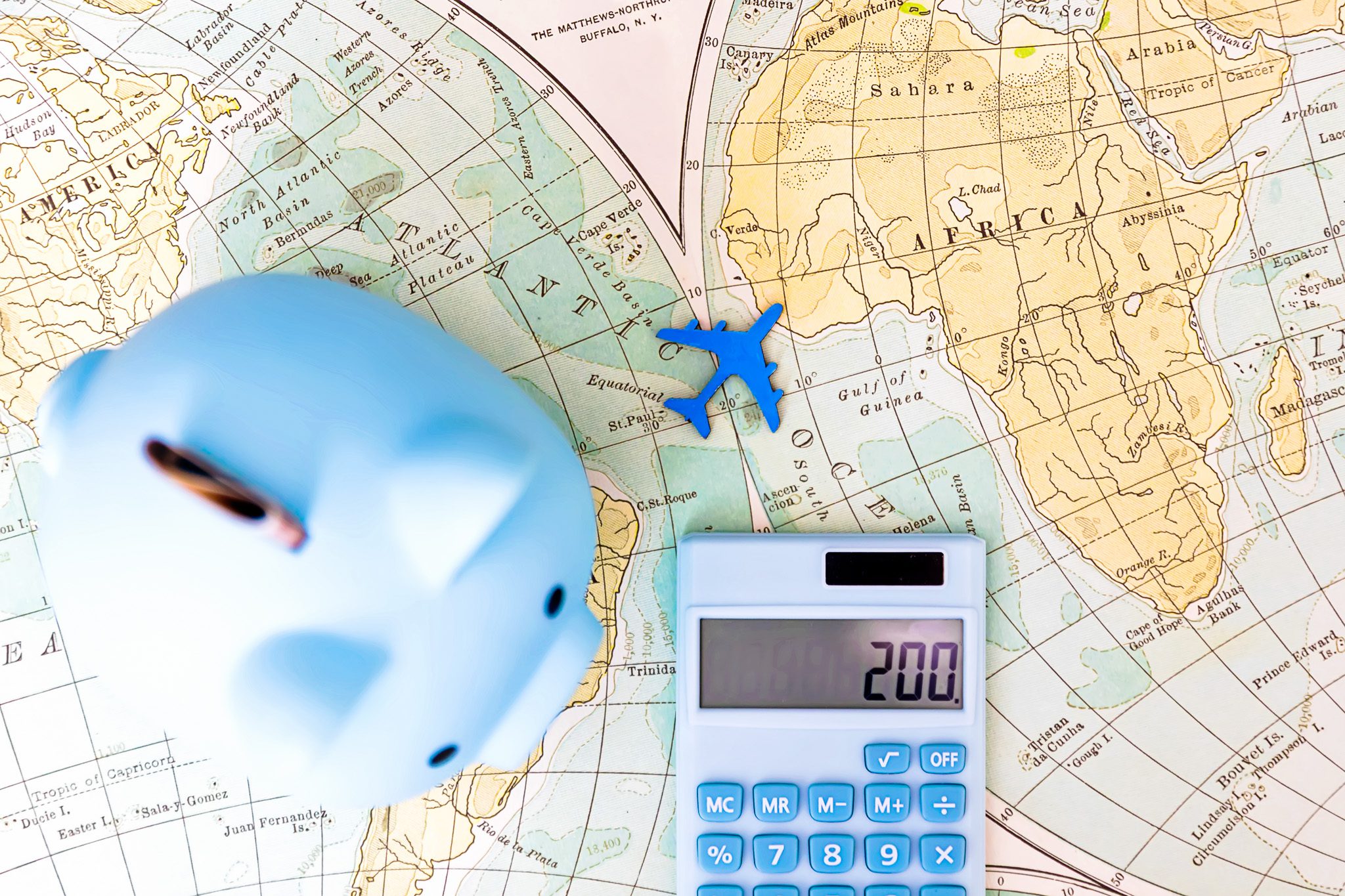 Piggy bank, toy airplane, and calculator on a world map