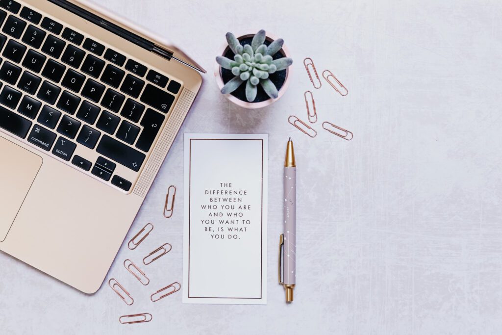 A motivational quote beside a laptop, pen, and clips