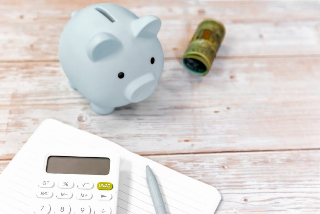 Piggy bank beside a roll of cash, a calculator, and a notebook