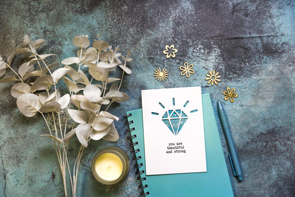 A motivational quote resting on top of a notebook, placed next to a candle and flowers