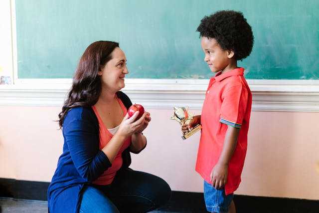 A teacher looking at her student while holding an apple