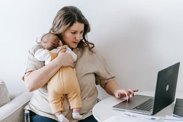Woman working on laptop with baby on shoulder