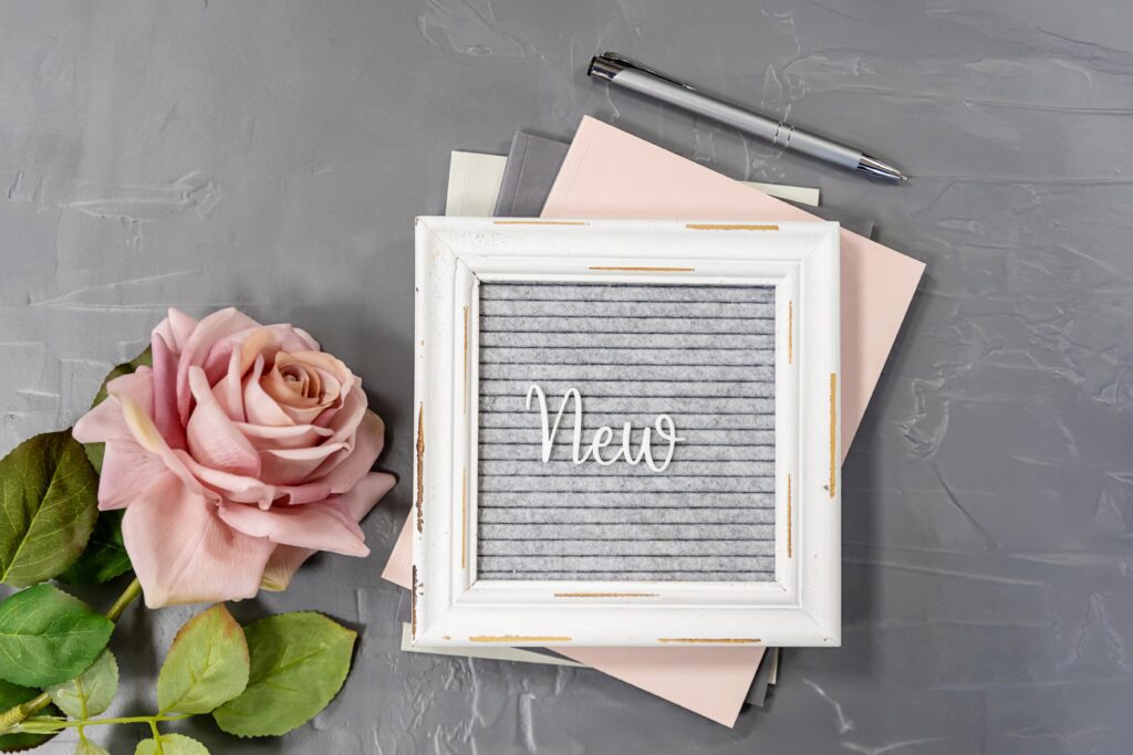A sign that says “New” placed on top of notebooks next to a flower