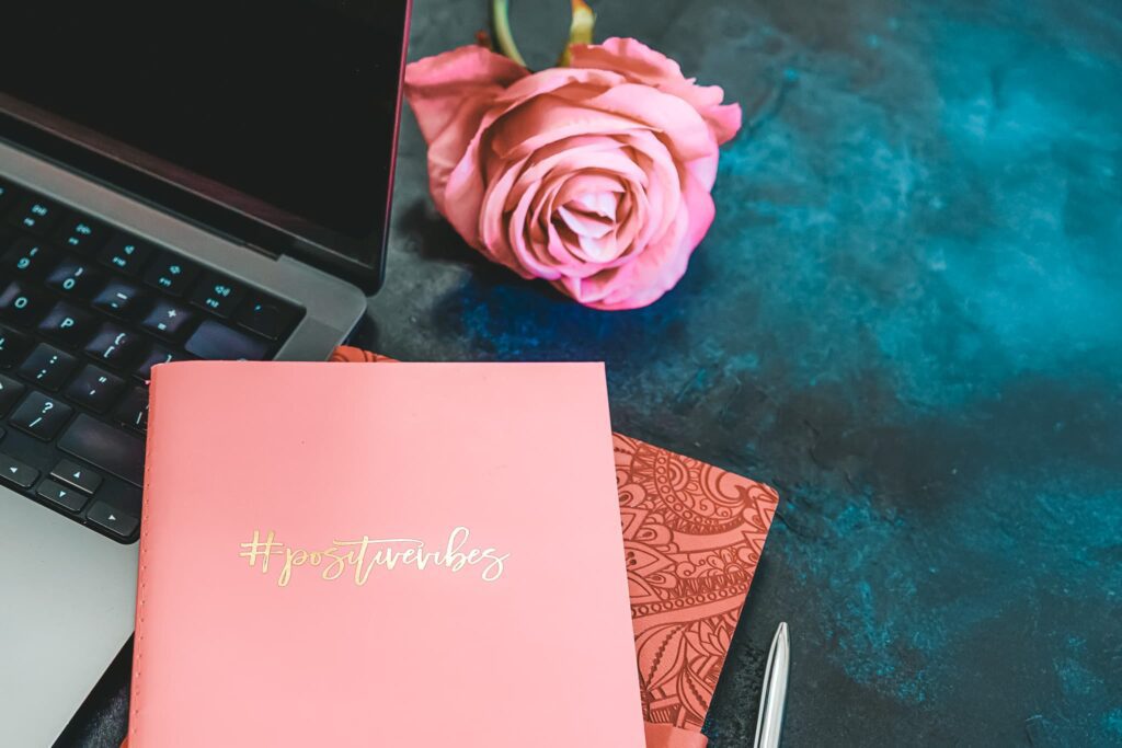 A notebook reading “positive vibes” placed near a laptop