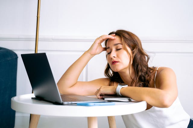 Woman with eyes closed lying on a coffee table, with a laptop next to her