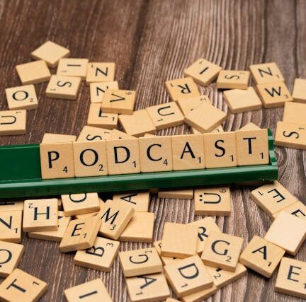 The word ‘podcast’ spelled out with Scrabble letter tiles on a wooden surface