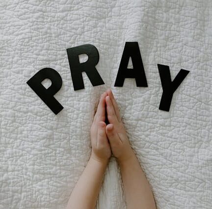 Praying hands on a bed with the word ‘Pray’ above them