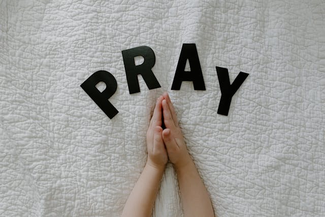 Praying hands on a bed with the word ‘Pray’ above them