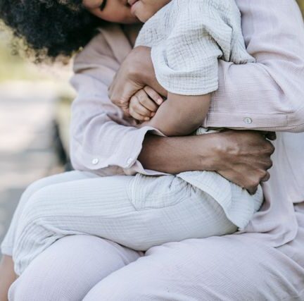 A mother hugging her daughter while sitting together on a bench outdoors in a park