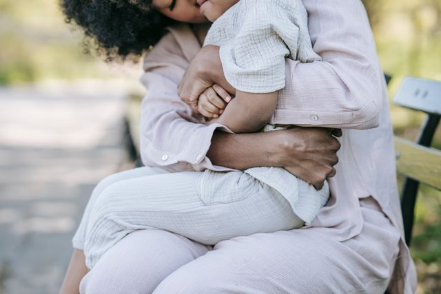 A mother hugging her daughter while sitting together on a bench outdoors in a park
