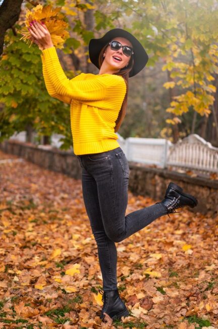 Smiling woman in autumn attire joyfully holding leaves in a park